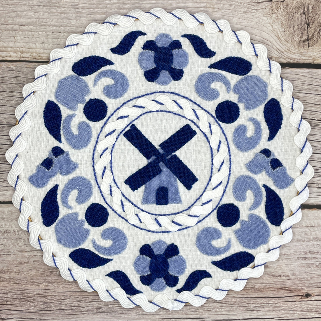 Dutch Porcelain Wool Applique Pattern.  Blue wool in two shades cut into traditional Dutch shapes such as windmill, tulips, and shoes. Pattern is placed in a hoop to mimic delft pottery.